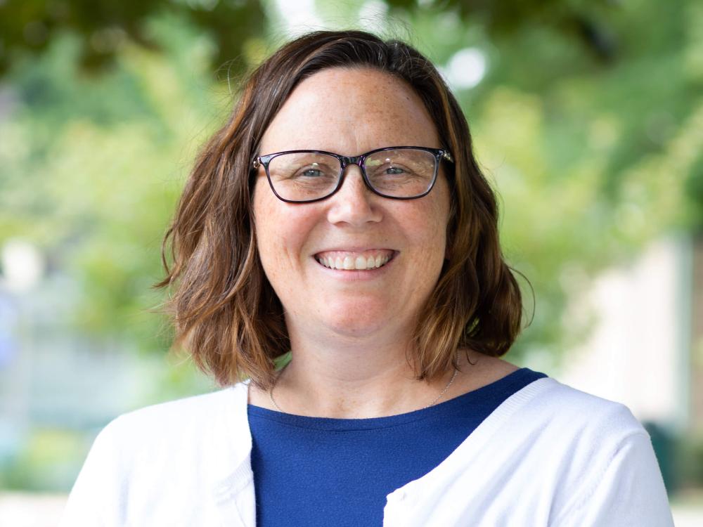 Jennifer Jewell wearing a blue shirt with a white sweater standing in front of trees